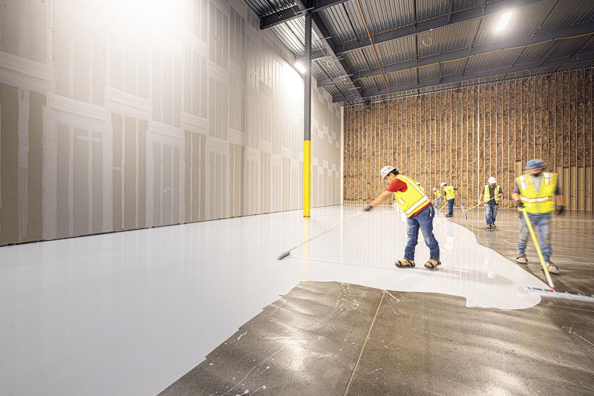 Workers in safety vests rolling a fresh white coating onto a large concrete floor