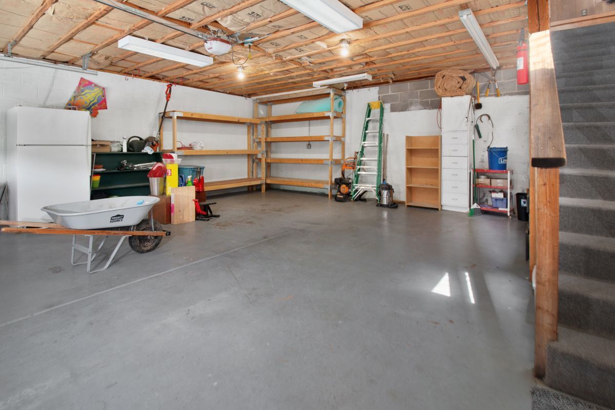 Residential garage with a smooth sealed floor, open shelving, a ladder and a wheelbarrow