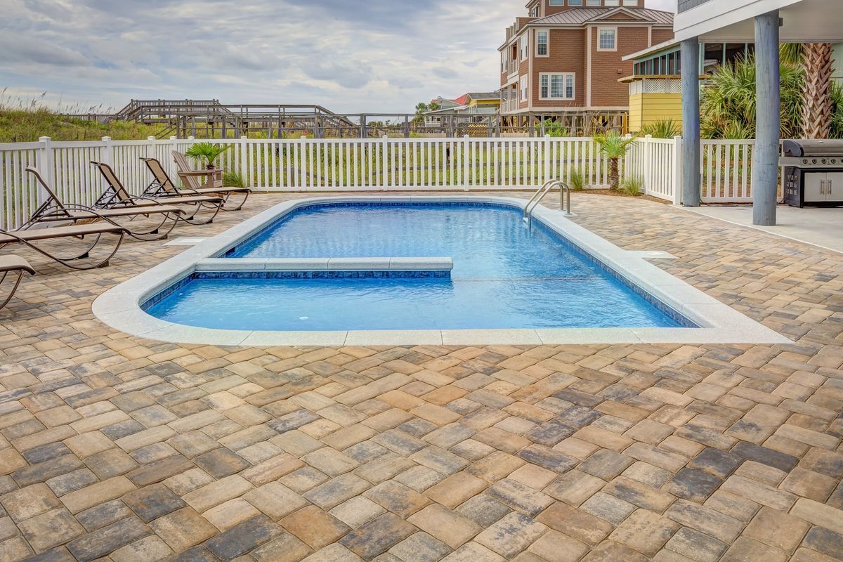 Backyard swimming pool with a wide textured deck, lounge chairs and a white fence